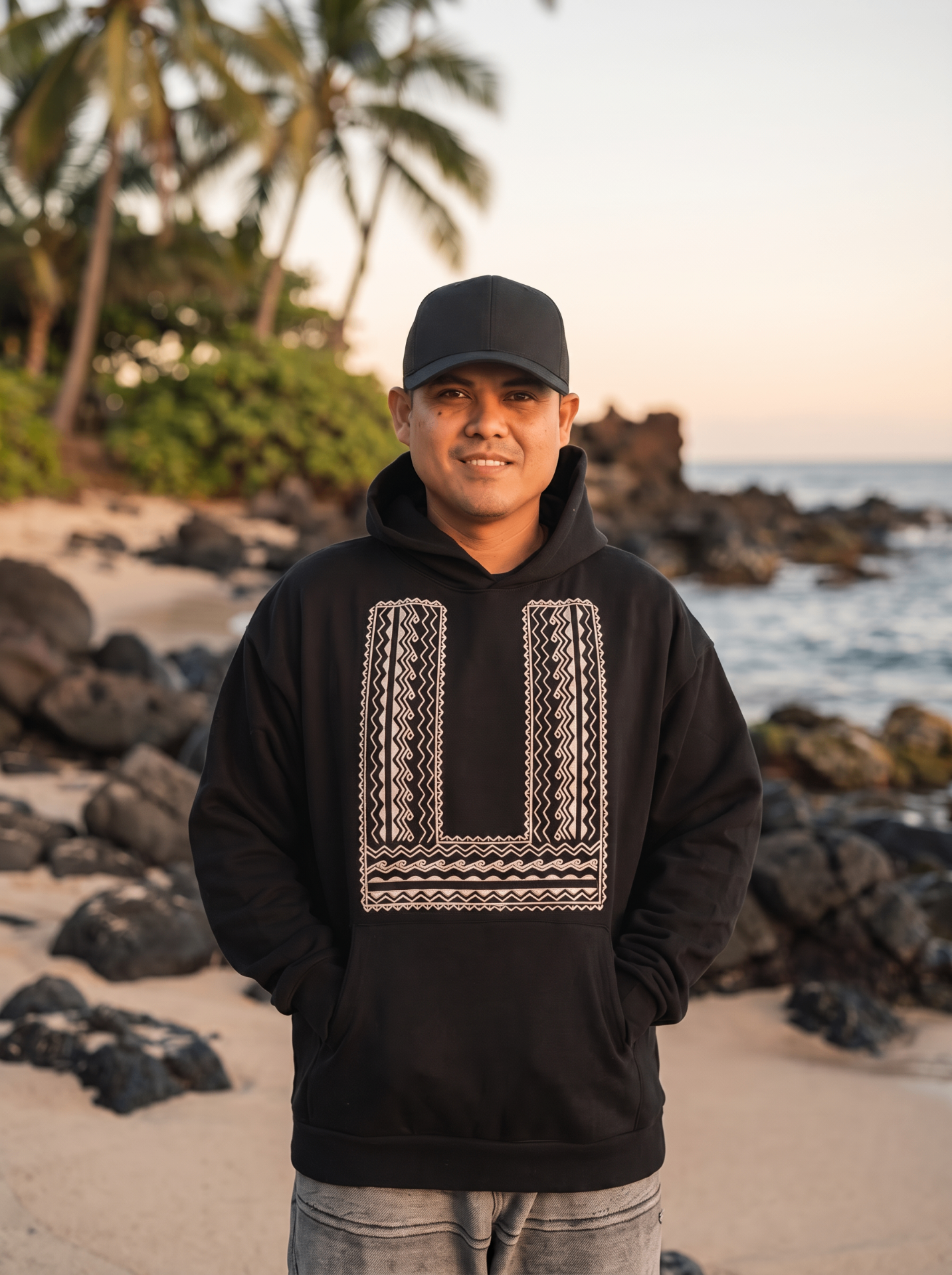 Isla Born lifestyle — model wearing black Isla Born hoodie and cap on a rocky island shore
